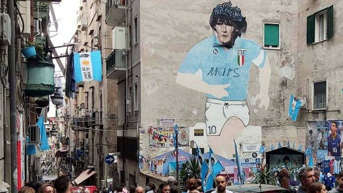 Murales di Maradona nei Quartieri Spagnoli di Napoli con folla e bandiere azzurre