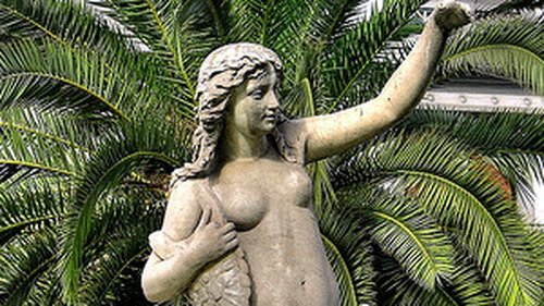 Statua della Sirena Partenope a Napoli davanti a una palma