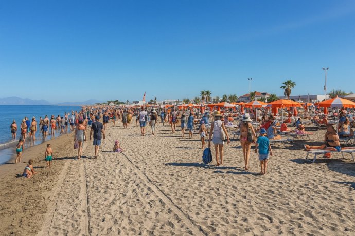 Spiaggia di Licola con ombrelloni arancioni, mare calmo e bagnanti lungo la battigia.