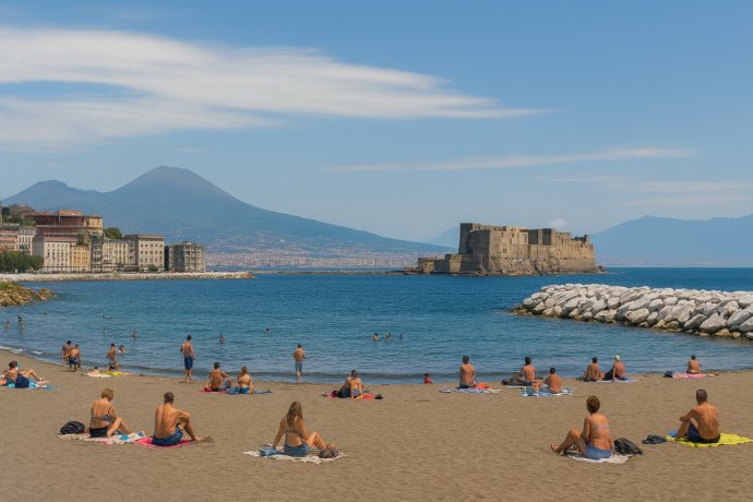 Mappatella Beach a Napoli con bagnanti, Castel dell’Ovo e Vesuvio sullo sfondo.