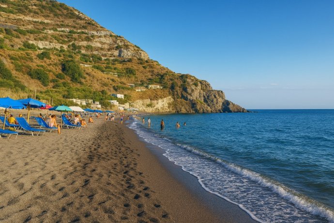 Ischia, Spiaggia dei Maronti: sabbia vulcanica, ombrelloni e scogliera; mare calmo al tramonto.