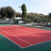 Campo da tennis all'aperto con recinzione e vegetazione.