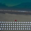 Vista dall'alto di una spiaggia con file di ombrelloni bianchi e uno rosso al centro.