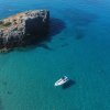 Vista aerea di una barca bianca vicino a una scogliera e una spiaggia con acque cristalline.