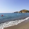 Spiaggia sabbiosa con mare calmo, persona in kayak rosso e colline in lontananza.
