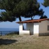 Casetta bianca con tetto rosso, immersa nel verde, vista mare e alberi circostanti.