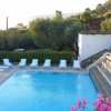 Piscina con lettini bianchi circondata da piante verdi e fiori rosa.
