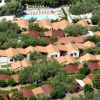 Vista aerea di bungalow con tetti rossi circondati da alberi e una piscina con sdraio.