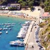 Spiaggia con ombrelloni e un molo con barche allineate in un porto.