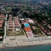 Vista aerea di un resort sulla spiaggia con edifici, piscina e ombrelloni.